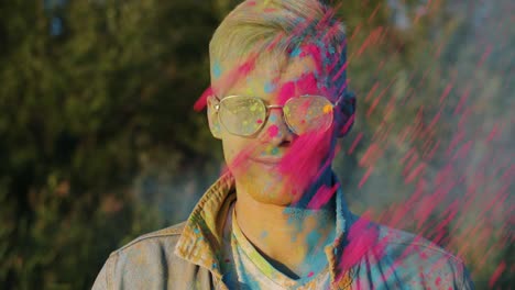 slow motion portrait of excited guy smiling while friends throwing powder paint at him having fun at holi festival