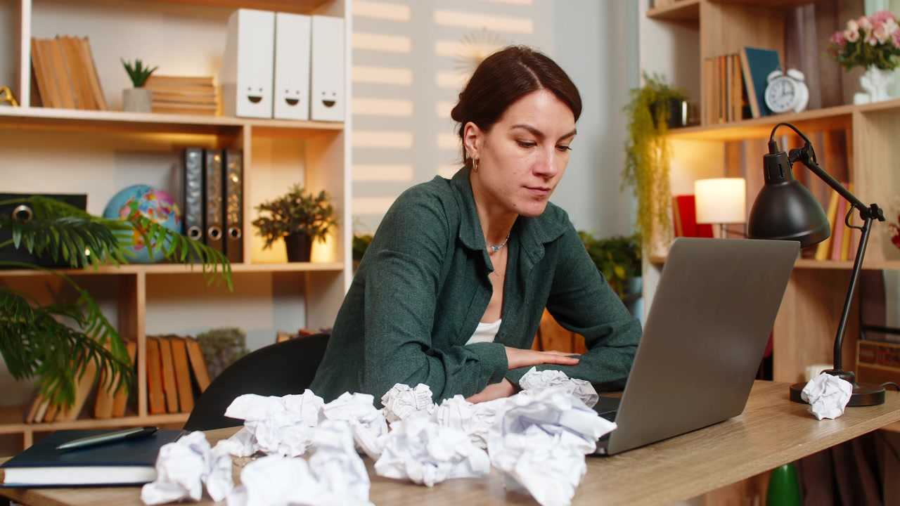 Young woman on home table brainstorming idea with laptop and crumpled paper during remote work task