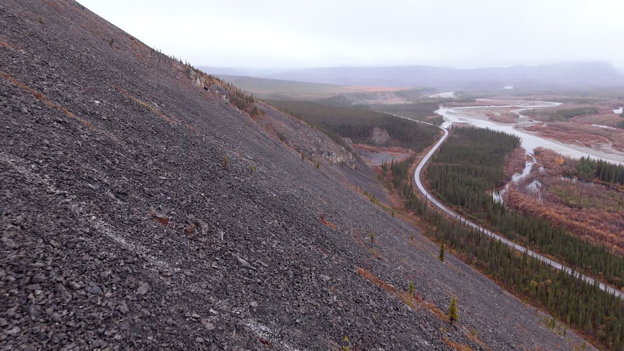 Rocky And Treeless Mountain Slope With Dempster Highway And River In Yukon, Canada. - aerial shot