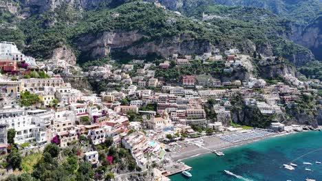 Slow-aerial-Reveal-over-Positano-beach-surrounded-by-tall-mountains,-lush-vegetation,-turquoise-water,-and-beautiful-coastal-homes,-Amalfi-Coast,-Campania-Region,-Italy,-Europe