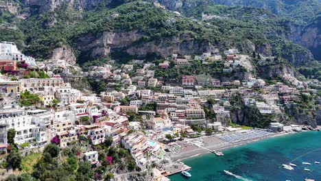 slow aerial reveal over positano beach surrounded by tall mountains, lush vegetation, turquoise water, and beautiful coastal homes, amalfi coast, campania region, italy, europe
