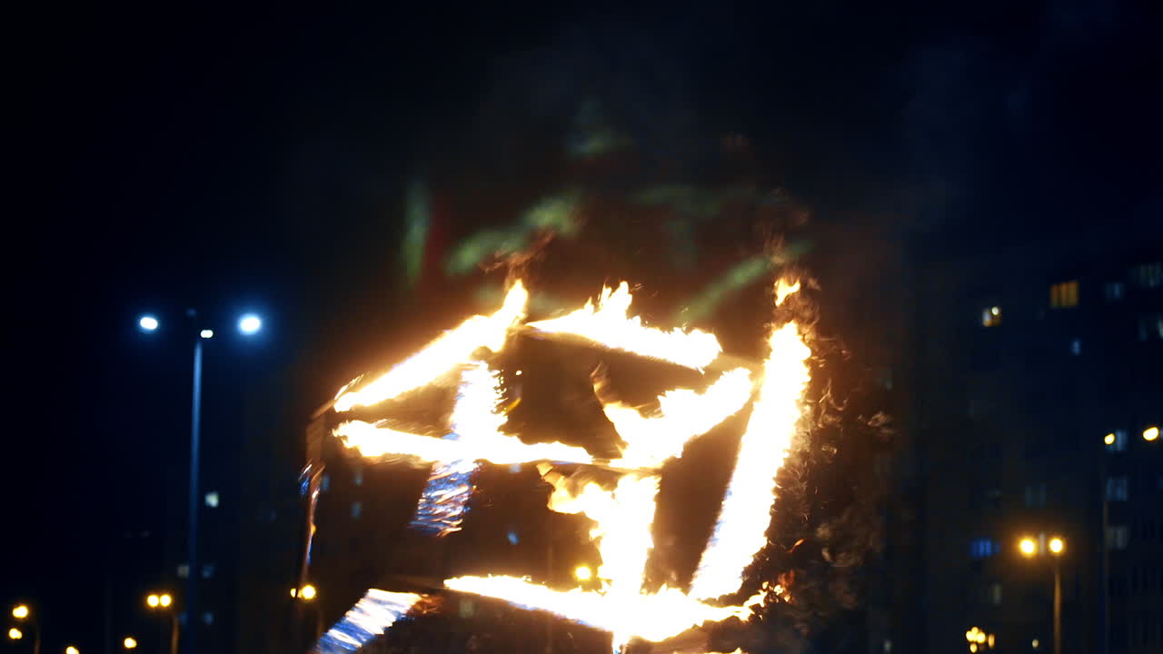 Male artist holds, turns and tosses the cube with burning sides. Dancer performs fire show at night.