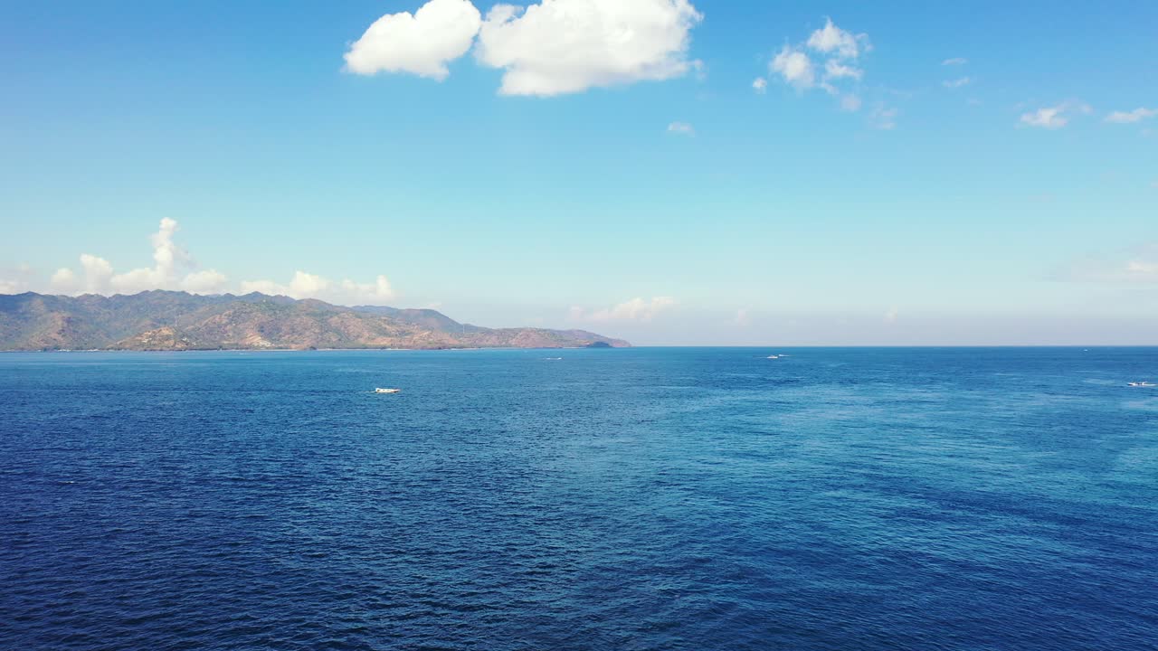 인도네시아의 흰 구름과 밝은 하늘 아래 높은 산이 있는 섬의 바위 해안 주변의 넓은 푸른 바다의 평화로운 풍경