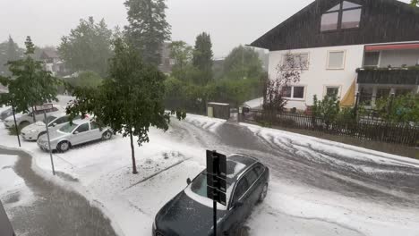 Environmental-disaster,-high-water-and-tons-of-hails-are-flowing-down-the-street-in-a-little-city-with-parking-cars-while-it's-still-raining-heavly