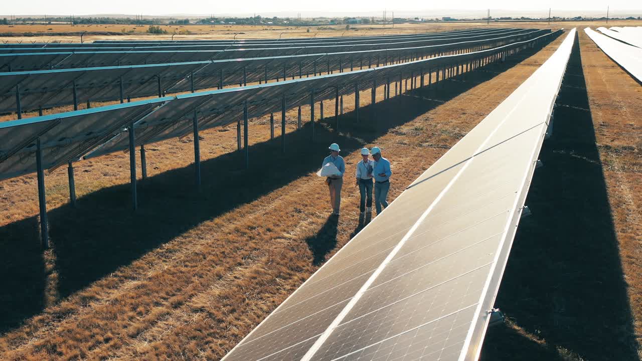 tomada de un dron de tres ingenieros de energía solar caminando en un parque solar