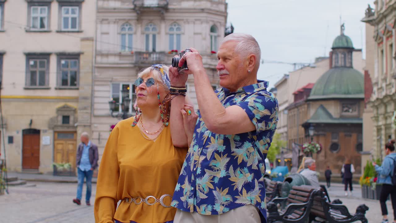 ancianos turistas elegantes hombre mujer caminando, tomando fotos con la cámara vieja en el centro de la ciudad de verano