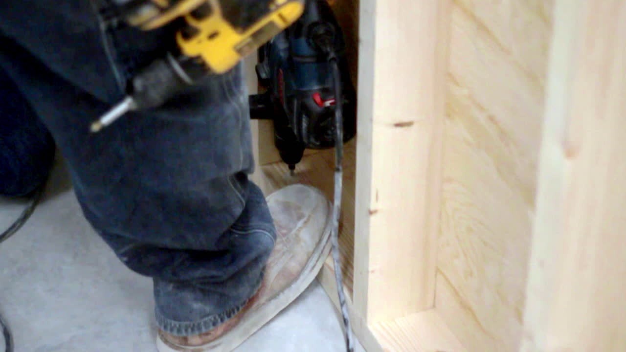 Focused precision as a worker carefully drills into wooden panels, surrounded by sawdust and tools, capturing a moment of silent concentration and craftsmanship.