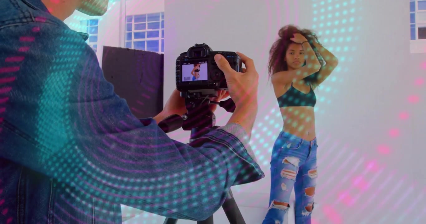 Fotografo solleva una fotocamera DSLR e fotografa una modella mentre luci proiettate danzano sulle pareti.