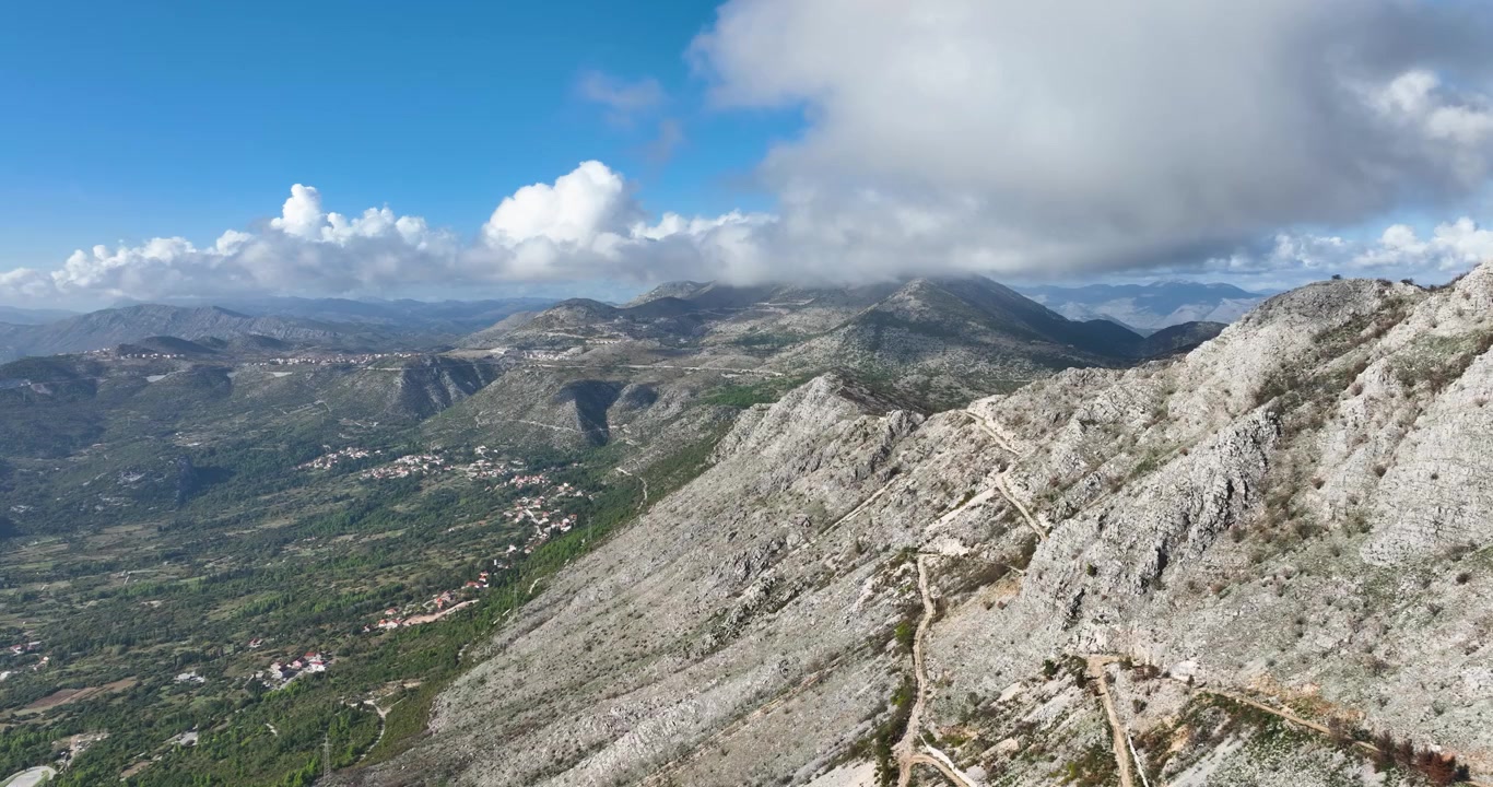 Panoramica aerea introduttiva delle aspre scogliere rocciose montane di Dubrovnik, pendii scoscesi che sfumano in valli erbose con case