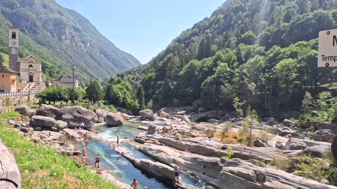A scenic view of Lavertezzo in the Verzasca valley on a sunny day with people gathering around the water.