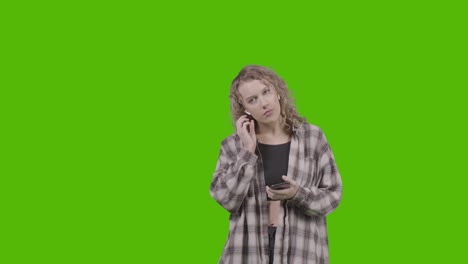 studio shot of young woman listening to music on mobile phone and dancing against green screen