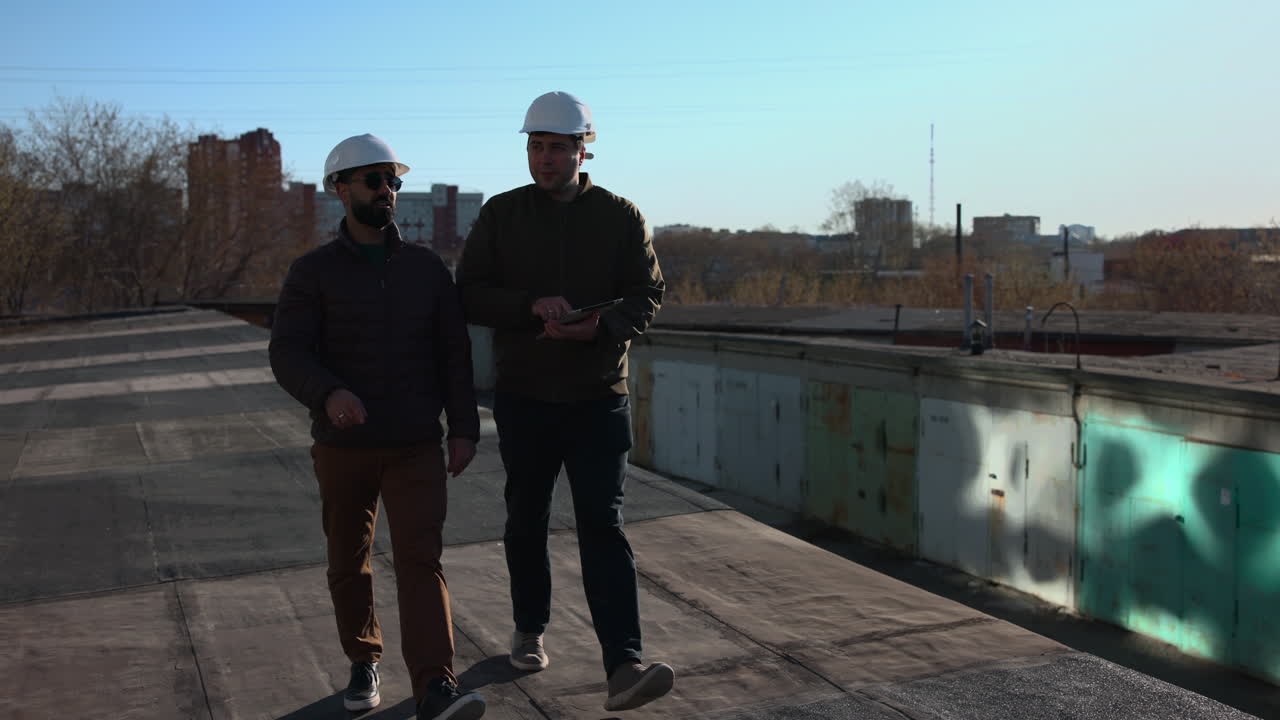 Two Professionals Walking Rooftop Together Discussing Timeline Tasks And Referencing Tablet For Coordination