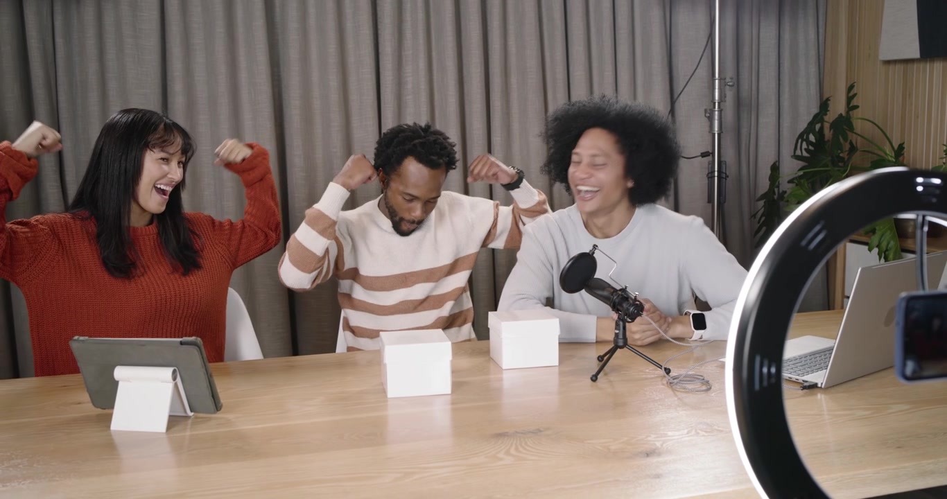 Diverse hosts filming through ring light framing phone, handling white boxes and recording segment
