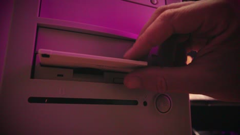inserting floppy disk into retro computer with pink light