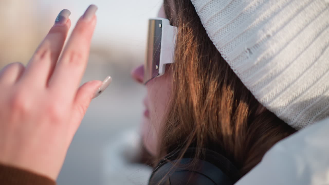 Close up side view of student wearing tinted goggles against winter sky and snowy weather while adjusting frame with manicured nails under warm sunlight and gentle breeze revealing radiant cheeks