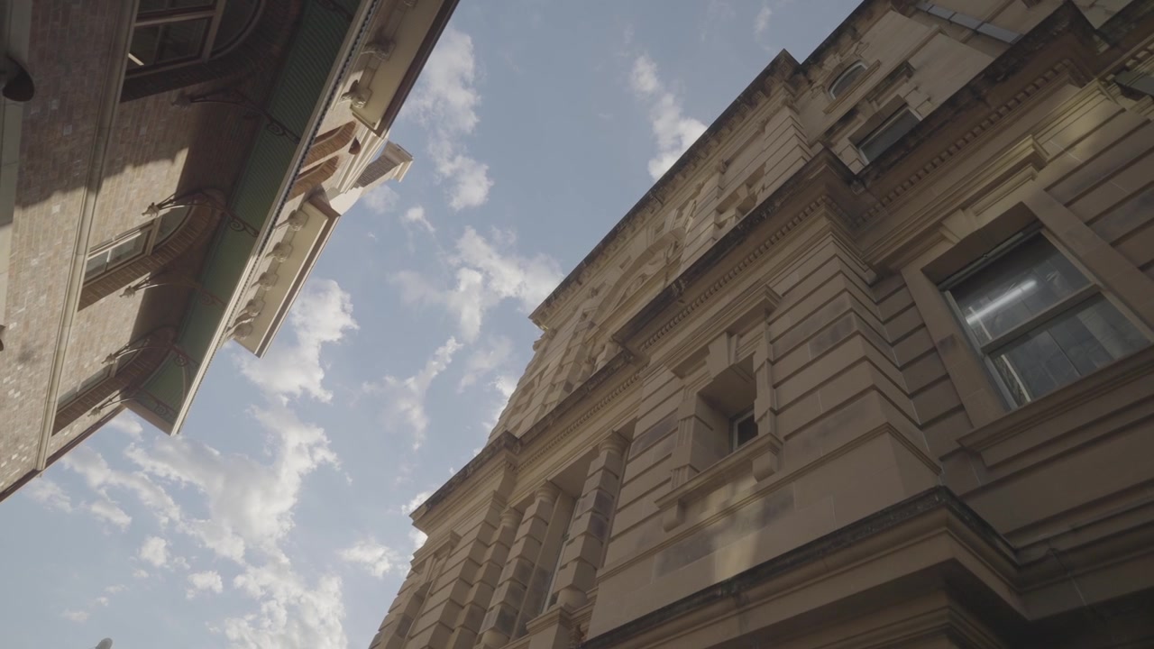 Una toma en contrapicado captura las molduras ornamentadas de las ventanas y la cornisa de un edificio histórico de arenisca