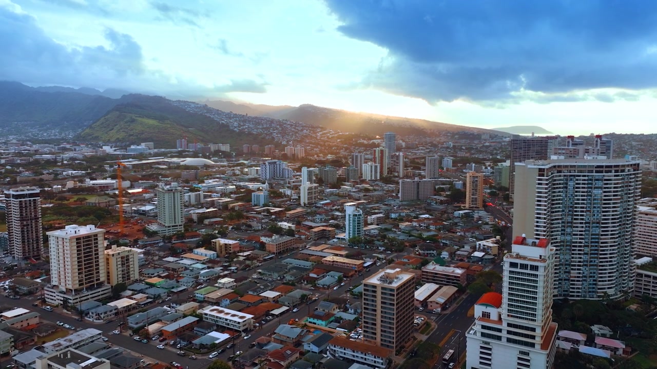 Volo sopra la zona prevalentemente a bassa densità di edifici di Honolulu, Oahu, Hawaii. Un cielo cupo e nuvoloso incombe sopra la città e le montagne