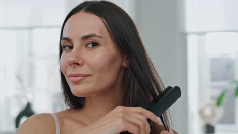 dama morena enderezando el cabello en el retrato del baño. modelo sonriente usando hierro
