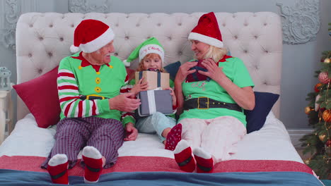 Abuelos-Mayores-Con-Nieta-Niña-Intercambiando-Regalos-En-El-Dormitorio-De-Casa-Cerca-Del-árbol-De-Navidad