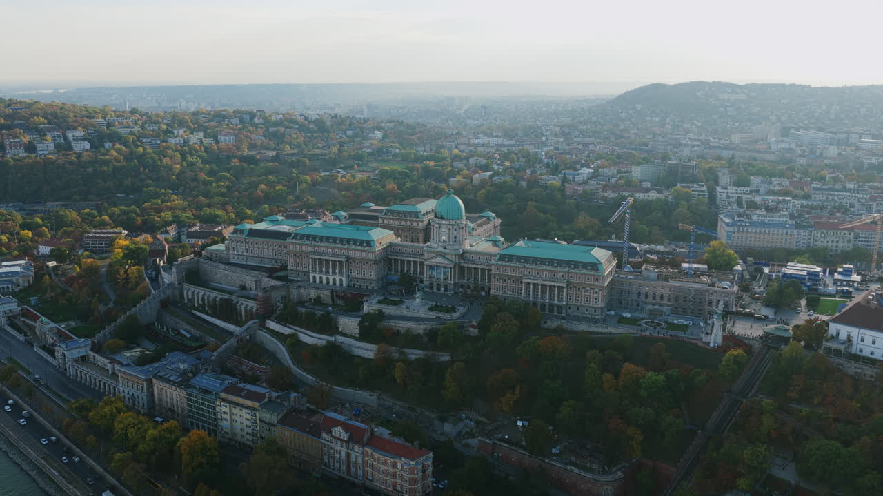 Wide drone view of Buda Castle and its terraces against the rolling Buda hills under soft morning light