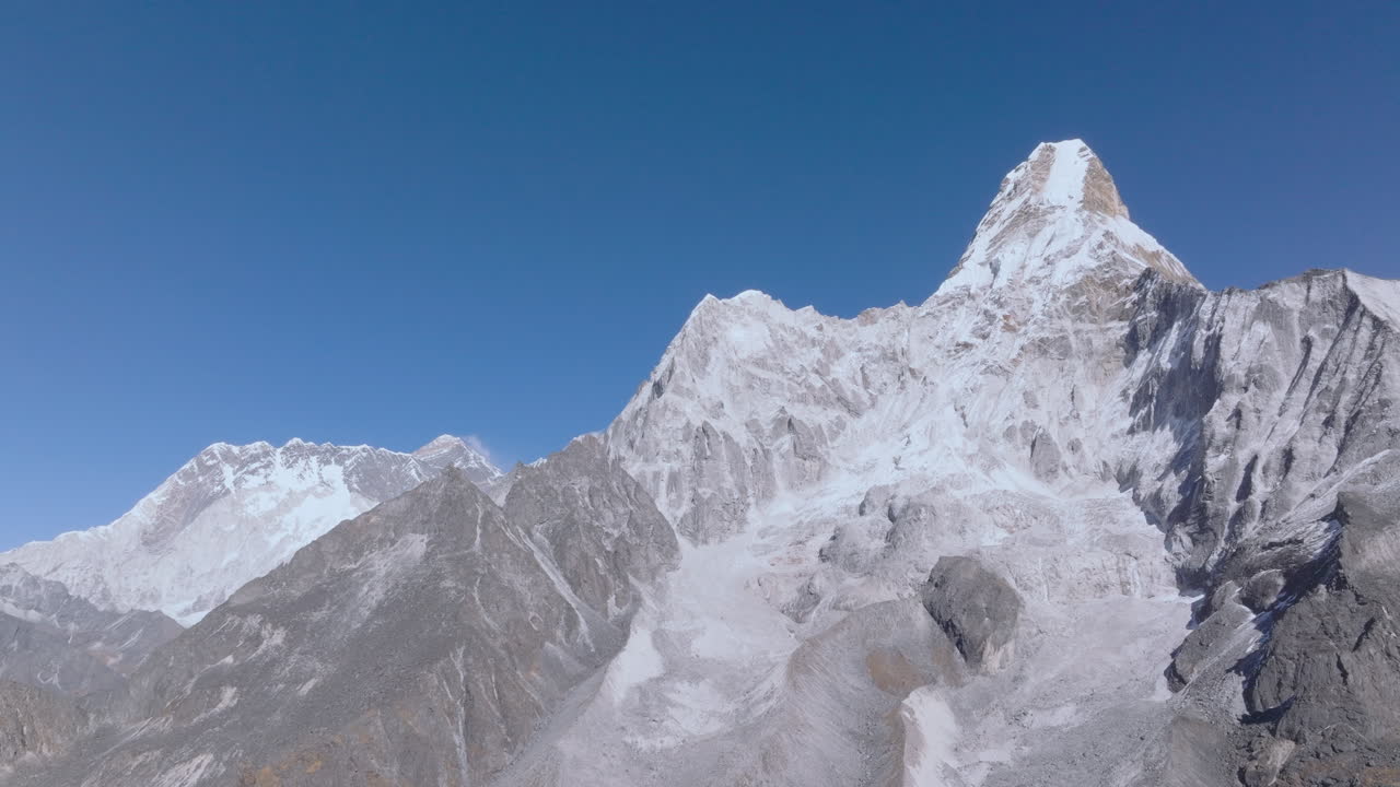 Gliding aerial drone view of the Himalayan mountains in Nepal, showcasing Mount Ama Dablam while subtly revealing Mount Everest in the backdrop. Wide alpine landscape for travel and documentary use