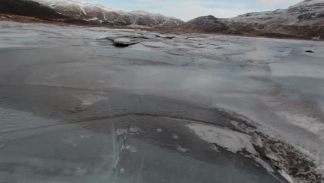 Flying-over-the-frozen-lake-by-the-snowy-mountains-of-Iceland---aerial