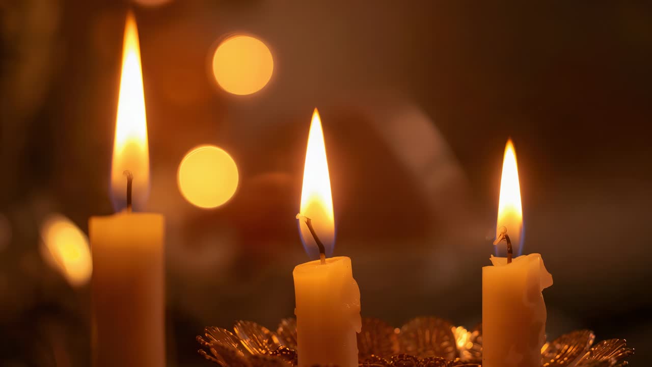 Candele tremolanti a tre pilastri che gocciolano cera in pozzanghere sul supporto di metallo sul caminetto, aggiungendo una luce accogliente