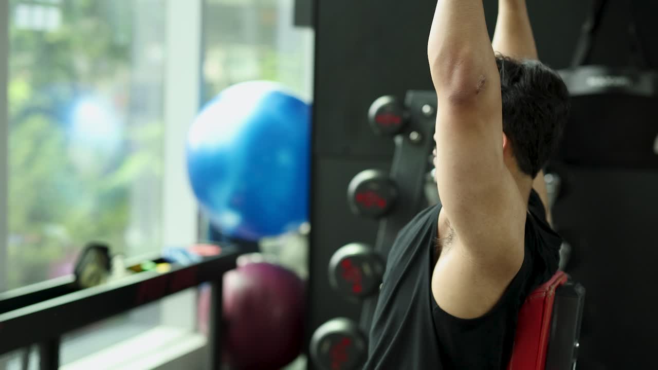 Atletische man die dumbbell shoulder presses doet in een modern, licht fitnesscentrum