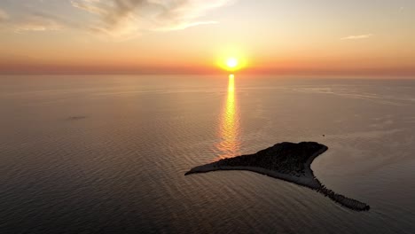 small islet in the sea - orange sunset sky with setting sun aerial