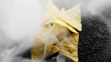 hand full of tortilla chips sitting on a bed of black rocks, surrounded by white smoke