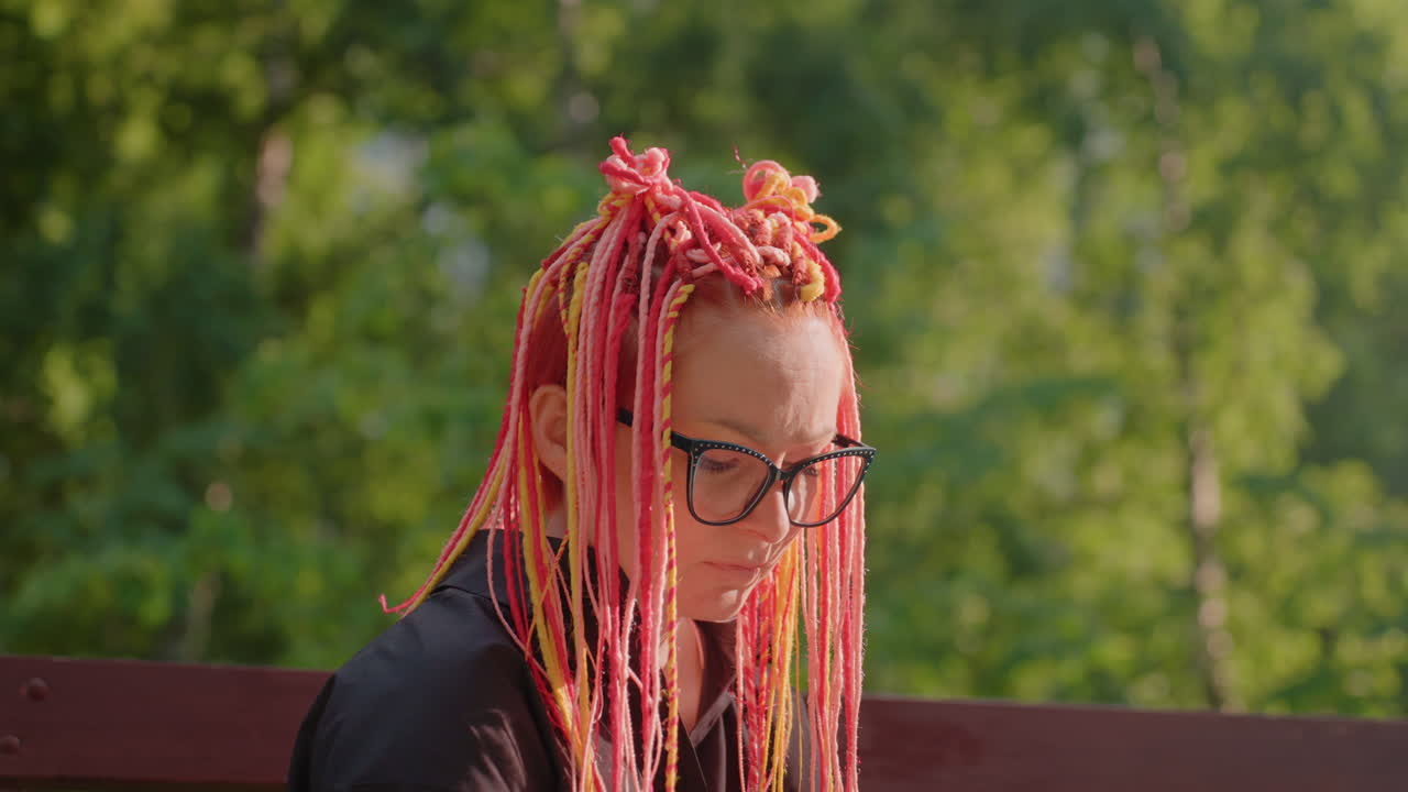 Mujer serena sentada en un parque durante el brillo del atardecer, figura femenina tranquila con trenzas en un entorno de parque apacible, mujer elegante con vibrantes trenzas rosas descansando con calma en un banco del parque al anochecer