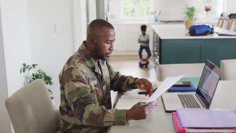 un feliz soldado afroamericano y su hijo sentados a la mesa, trabajando.