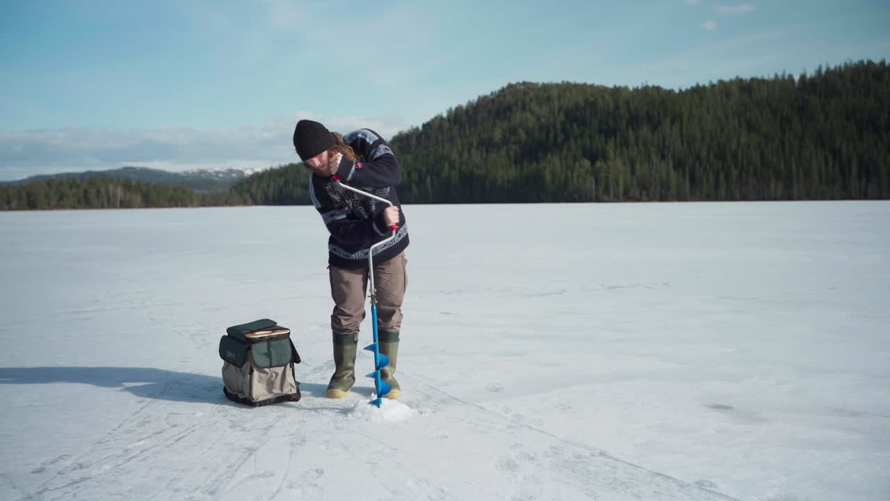 un hombre con un perforador de hielo de mano perforando un agujero en un lago congelado durante un día soleado