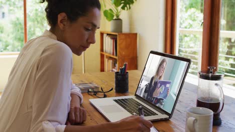 Mixed-race-businesswoman-sitting-at-desk-using-laptop-having-video-call-with-female-colleague