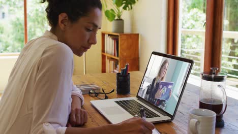 mixed race businesswoman sitting at desk using laptop having video call with female colleague