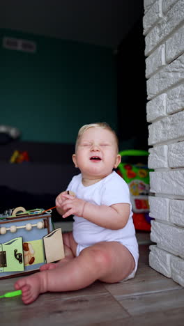 smiling baby boy sits on the floor with a toy in front of him. blond toddler pushes the toy trying to stand up. vertical video.