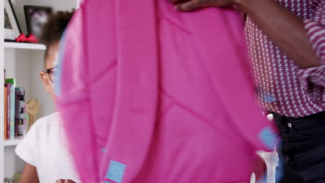 mother helping daughter to pack bag for school in bedroom