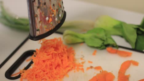 raising grater to show grated carrots on a cutting board