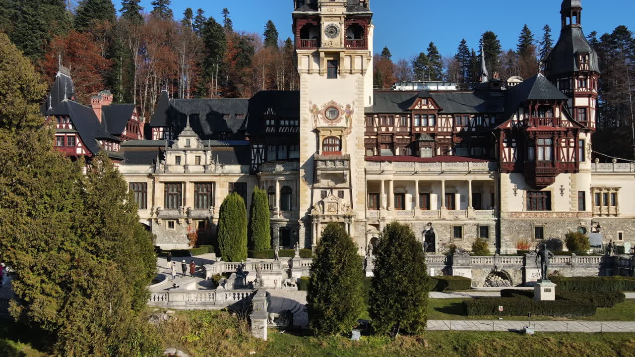 Aerial drone view of The Peles Castle in Romania. Castle with gardens in Carpathians, tourists, forest around it. Slow motion