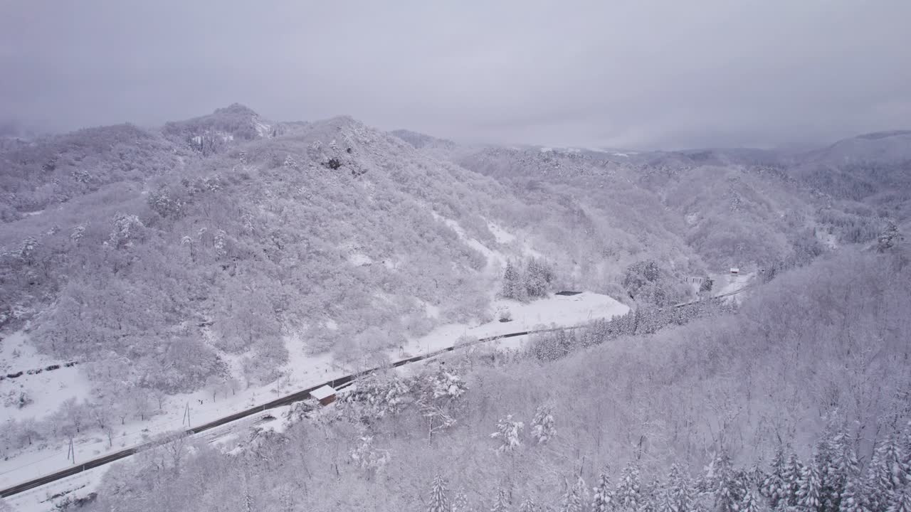 Aerial drone footage of snow-covered mountains and forest valleys during winter, showing a peaceful and scenic landscape