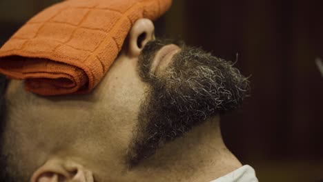 closeup of a man in a barber shop having his mustache and beard trim using razor while covering his eyes