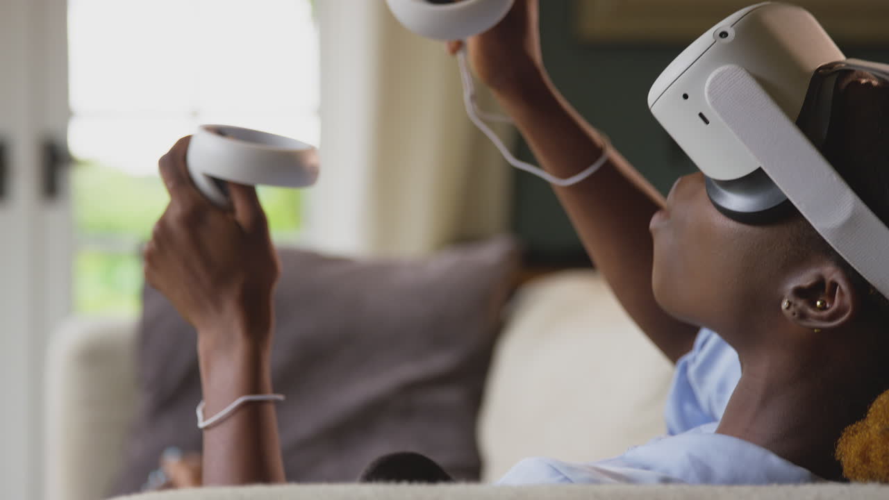 Donna sdraiata sul divano a casa che indossa un visore VR con controller e con tecnologia AR.