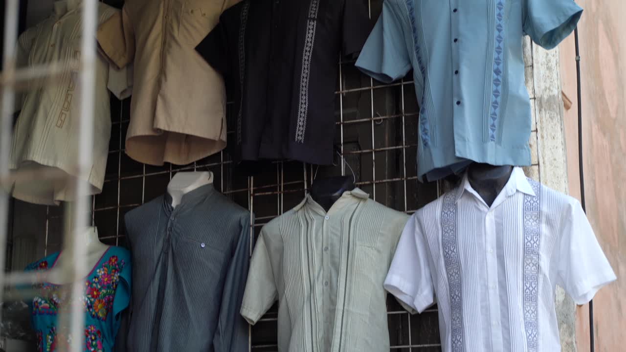 Camera pans down showing assortment of street vendor’s display of guayabera men’s shirts in Merida Mexico