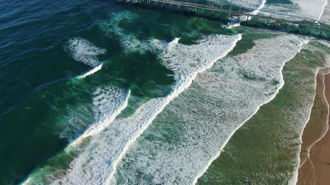 descendiendo sobre las olas, la playa de perros de la costa dorada y el embarcadero de bombeo de arena al atardecer