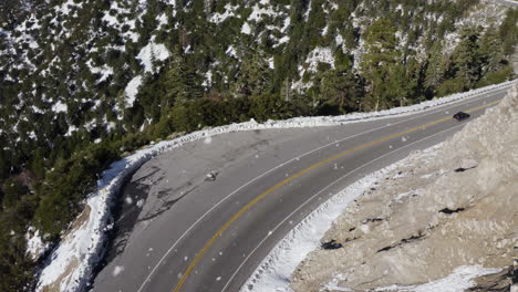 black car driving on mountain top road in snowy landscape, aerial view