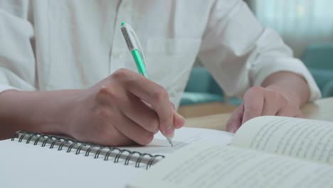 hombre de la mano estudiante escribiendo en el cuaderno en la mesa mientras estudia en casa