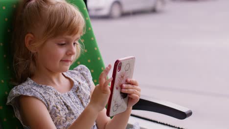 niño atractivo sonriente niña niño en el tren de la ciudad, tranvía o autobús usando teléfono inteligente charlando con amigos