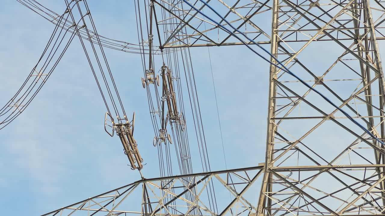 Closeup view of suspension clamps with vibration dampers supporting high-voltage conductors on a lattice steel tower, engineered to reduce wind stress and protect lines
