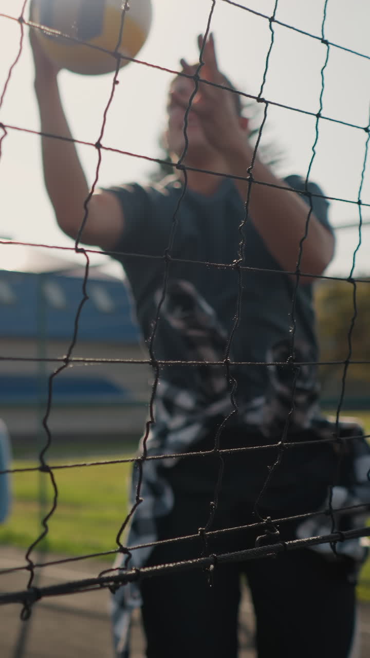 Volleyball player serving ball to lady in training session lady slams it back as player jumps to catch it, background shows other player in blur with volleyball net in outdoor court