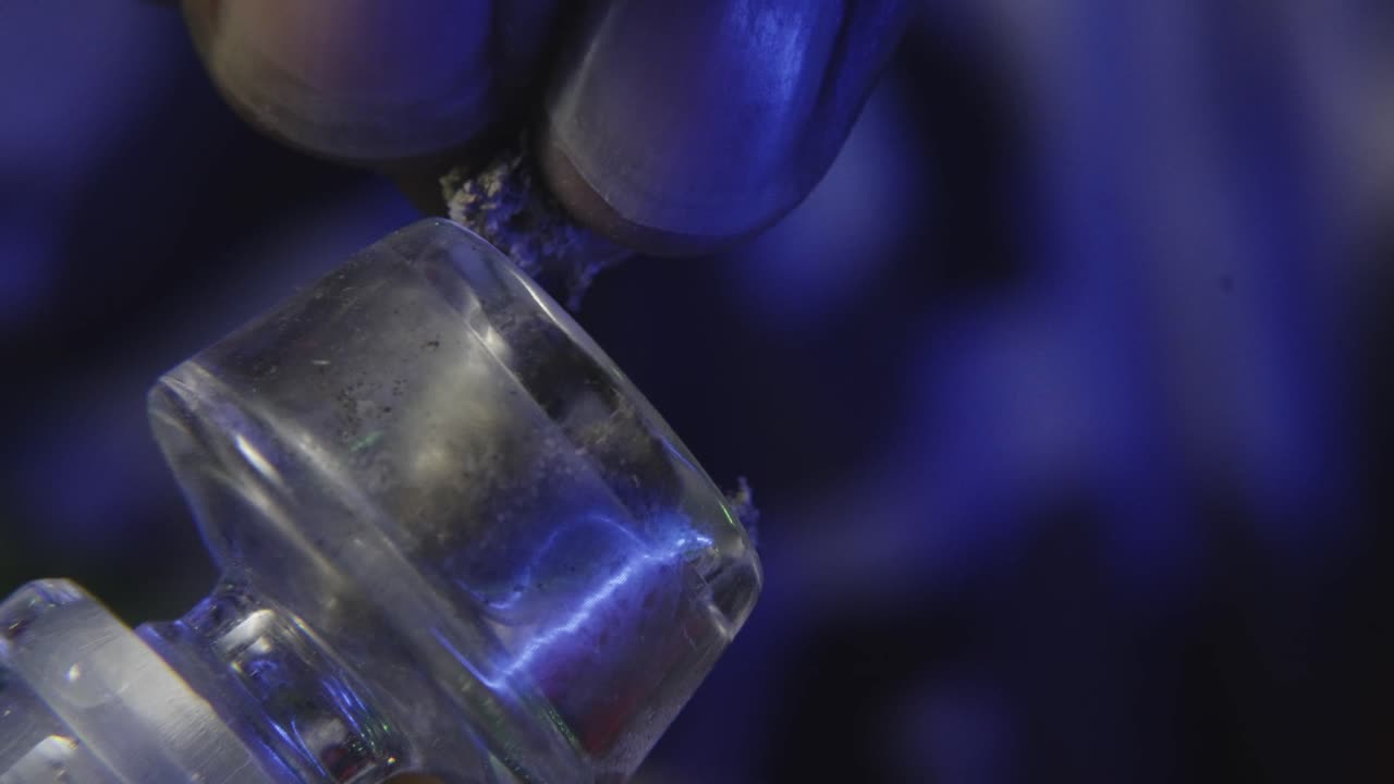 un primer plano de un hombre negro rompiendo un brote de cannabis para fumarlo de una pipa de marihuana